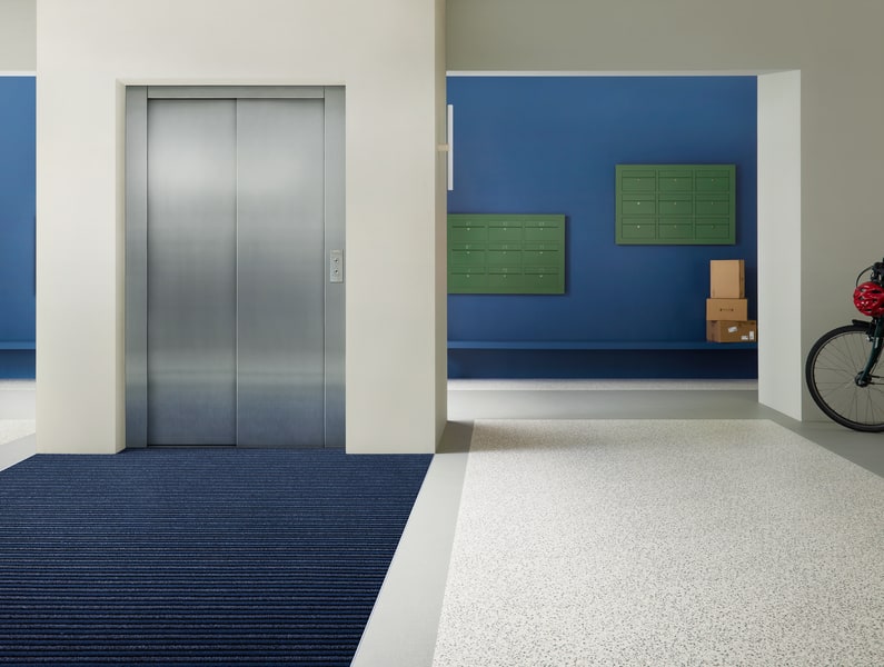 Blauwe schoonloopmat bij de lift van een appartementsgebouw