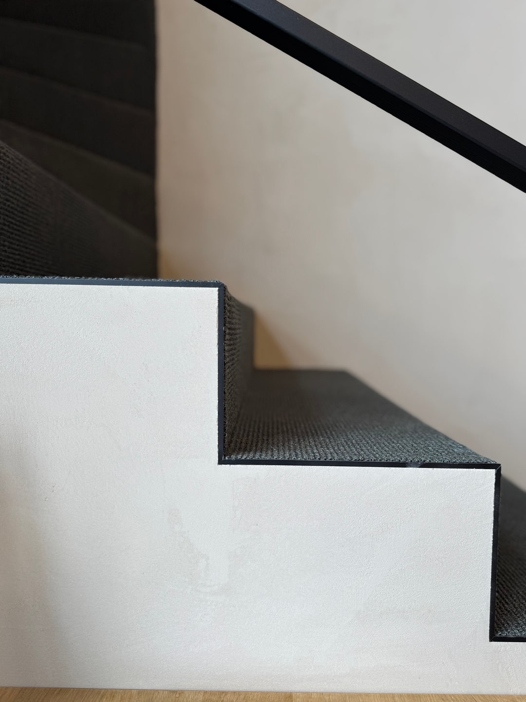 Detail van antraciet tapijt op strak afgewerkte treden met zwarte leuning